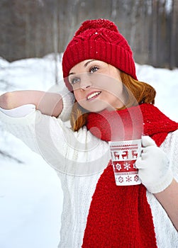 A woman in a white sweater and red scarf and hat is holding a winter cup close up. Winter and christmas time concept