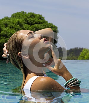 Woman in white swimsuit posing near swimming pool. Beautiful stylish tan girl. Summer day on island. Phuket, Thailand.