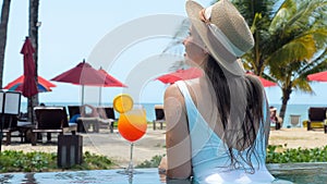 Woman in white swimwear and hat relax in swimming pool enjoy beautiful sea view with sun beds at sandy beach with