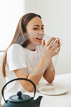 A woman in white t-shirt enjoying a cup of tea at home