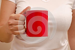 A woman in a white T-shirt holds a red mug in her hand. Empty mug for lettering or logo