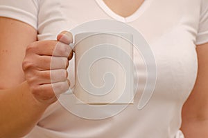 A woman in a white T-shirt holds a white mug in her hand