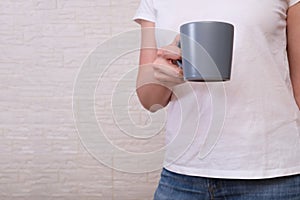 A woman in white t-shirt and jeans holding a cup of crisp hot beverage in hands in the morning, copy space