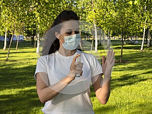 A woman in a white t-shirt and protective face mask is cleaning her hands with spray sanitizer