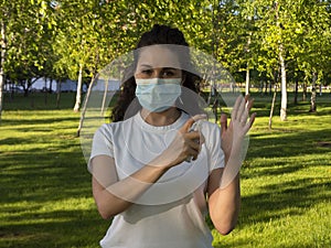 A woman in a white t-shirt and protective face mask is showing how to use hand sanitizer