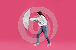 Woman with white umbrella caught in gust of wind on pink background