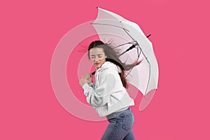 Woman with white umbrella caught in gust of wind on pink background