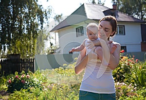 Woman in white vest holding baby on arms outdoors