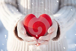 A woman in a white warm sweater holds a red heart with her hands against the background of a winter landscape and snow