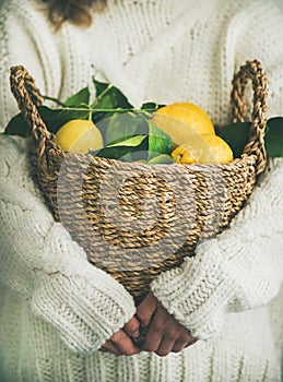 Woman in white woolen sweater holding basket of fresh lemons