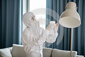 Woman in white workwear and protective eyeglasses disinfecting the lamp