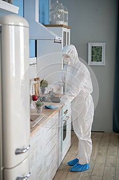 Woman in white workwear and protective eyeglasses disinfecting the surfaces