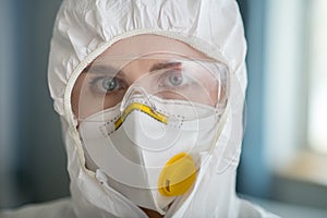 Woman in white workwear and protective eyeglasses looking determined
