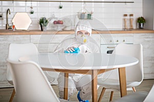 Woman in white workwear and protective gloves doing disinfection in the kitchen