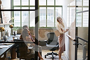 Woman at whiteboard in team meeting, seen through open door