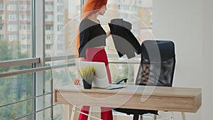 A woman who came to work and starts her working day in the office by the panoramic windows working at a computer.