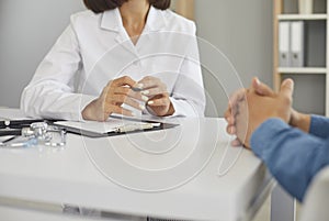 Woman who works as doctor sitting at desk and having conversation with her patient