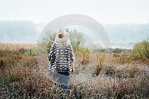 Woman in wide-brimmed felt hat and authentic poncho standing in high brown grass at foggy morning