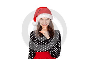 Woman wide eyed asking for silence or secrecy with finger on lips. emotional girl in santa claus christmas hat isolated on white b