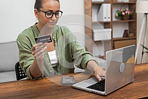 woman wields a credit card beside her laptop, efficiently handling online payments and shopping