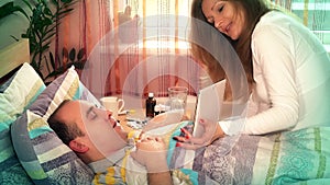 woman wife with tablet computer entertain her sick husband man in bed