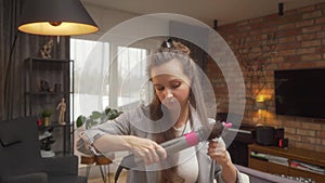 A woman winds curls on a brush attachment using a multi-styler hairdryer at home