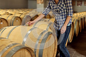 Woman winemaker checks oak wine barrels in which red wine is age