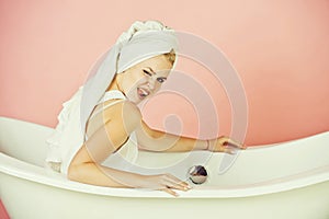 Woman winking with towel turban sitting in white bathtub