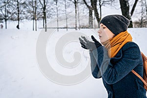 A woman in winter clothes blows snow off her palms in gloves