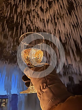 Woman in winter clothes holding glass of champagne in cove with glacier