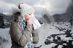 Woman in winter clothes holding a tissue to her nose