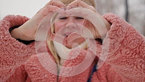 woman in winter clothes makes a heart symbol with her hands and smiles