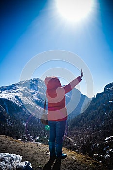 A woman in winter clothing standing on top of the rock of a snowcapped rocky mountain. Rear view. Deep Snow and Blizzard all