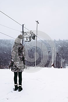 Woman in winter coat standing on slope near loop-line ski lift during snowfall. beautiful winter view in snowy weather. Mountain photo
