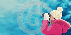 Woman in winter, female photographer takes picture on digital camera outdoors on blurred snowy forest background, blank copy space