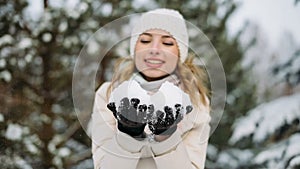 Woman in winter hat blows off snow from hands