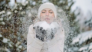 Woman in winter hat blows off snow from hands