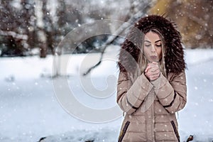 Woman in winter snow day blow on her cold hands