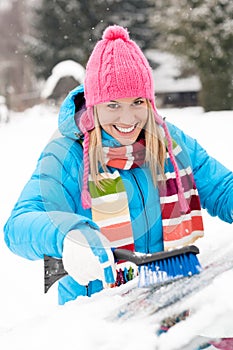 Woman wiping car windshield using brush snow