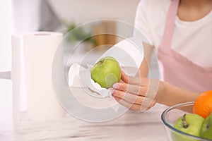 Woman wiping green apple with paper towel in kitchen, closeup