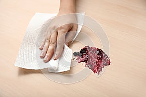 Woman wiping spot of jam on wooden table with paper towel