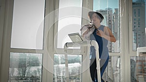 Woman is wiping sweat with towel during intense fitness workout on treadmill. Female athlete is exercising on smart trainer at hom