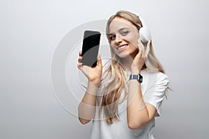 woman in wireless headphones with blank screen on phone on white background
