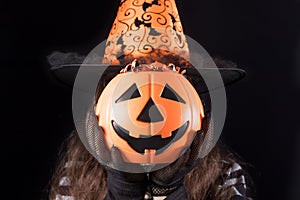 A woman in a witch costume in a hat holds a bucket of candy instead of a head. Halloween people.