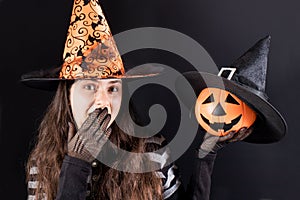 A woman in a witch costume holds a pumpkin lantern jack and covers his mouth with his hand. Halloween sale