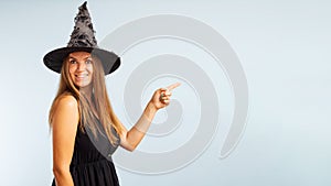 Woman in witch costume pointing with finger at copyspace side and looking at camera on blue background. Happy Halloween