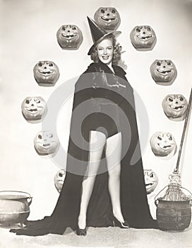 Woman in witch costume surrounded by carved pumpkins