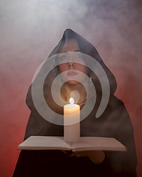 Woman witch is holding a burning candle. Mysterious smoke