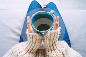 Woman in woolen cozy sweater warming cold hands with a mug of hot tea. Woman holding cup of tea.