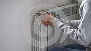 Woman in woolen sweatshirt tries to catch stream of warm air from central heater touching device